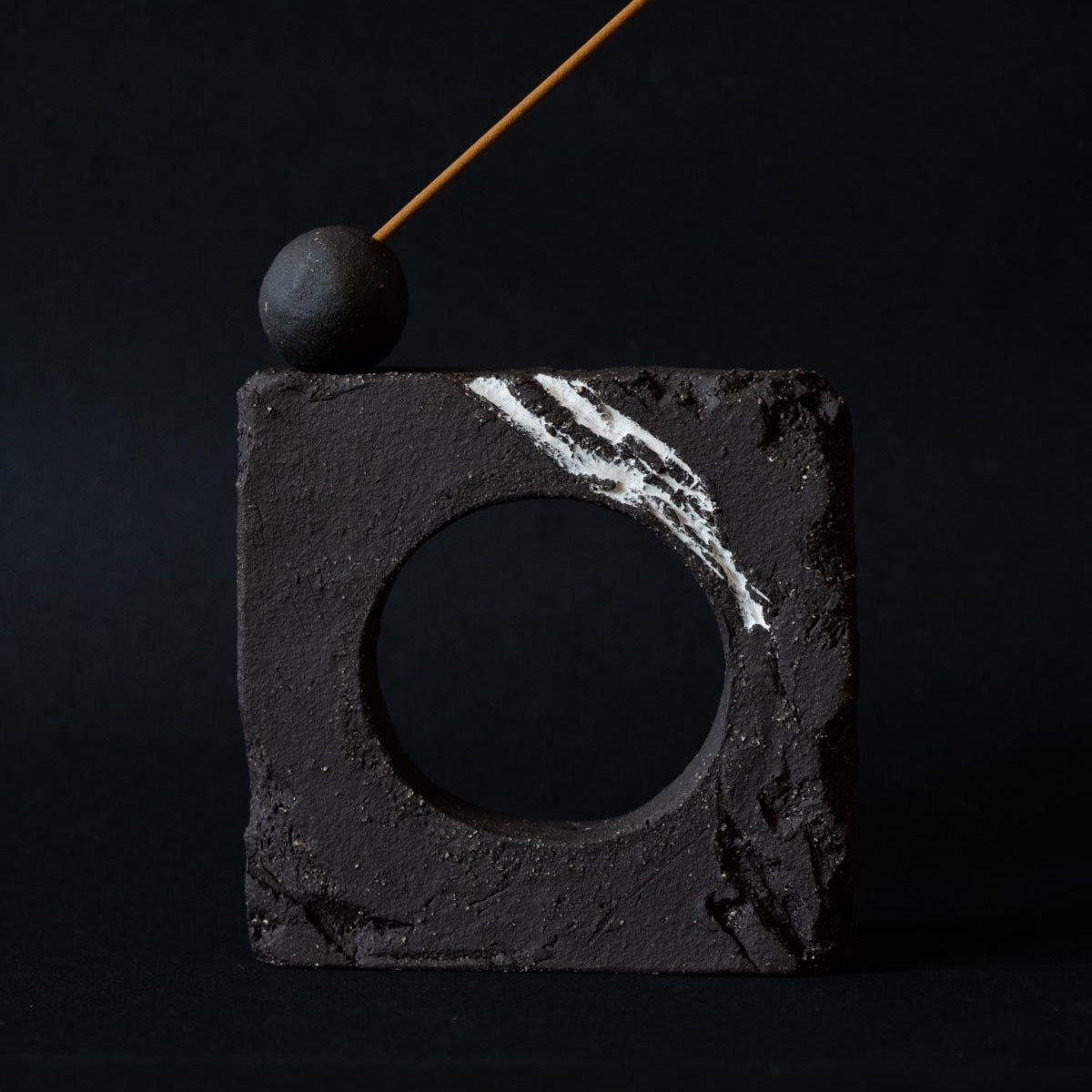 Black stone sculpture with a circular cutout and a small sphere on a black background