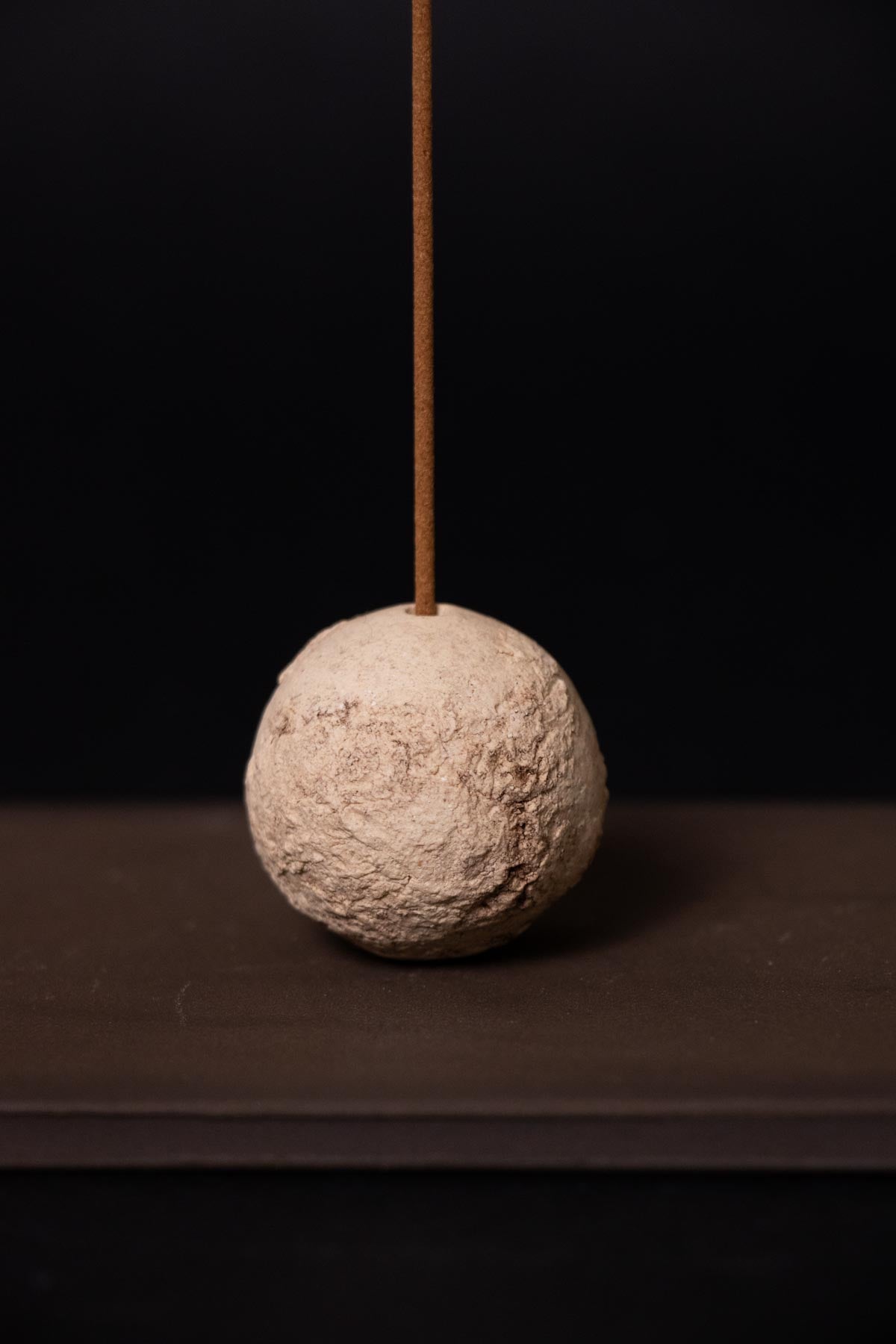 Textured sphere with an incense stick on a dark background