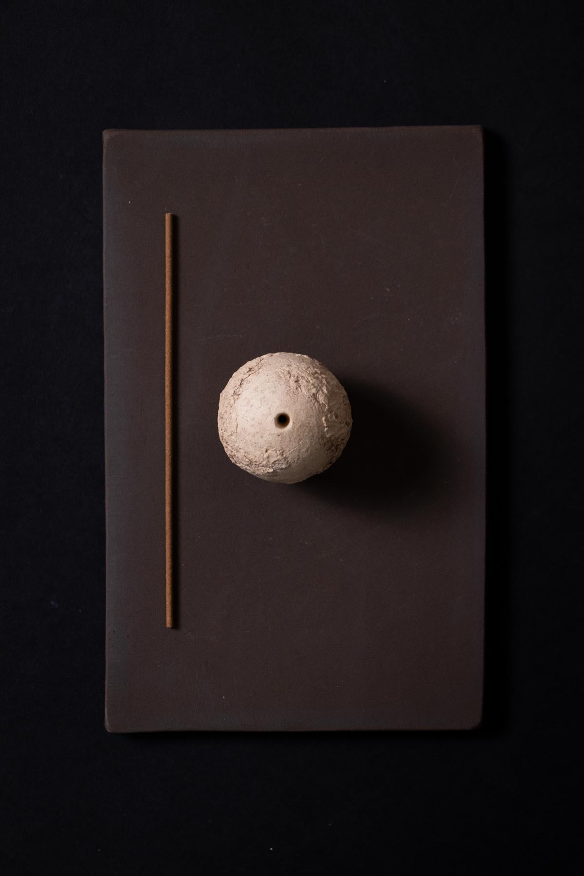 view from above of an artistic incense holder. Stoneware ceramics. Cream sphere with organic texture. Incense stick lying on the side. brown ceramic tray.