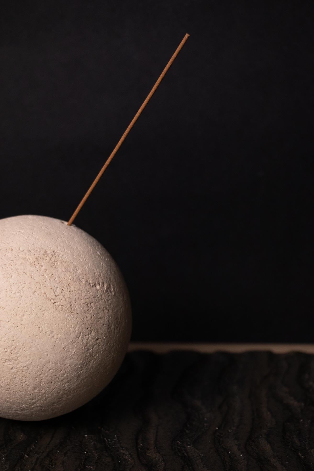 White ceramic sphere with an incense stick on a dark background. Close up of Claire Lune incense burner.