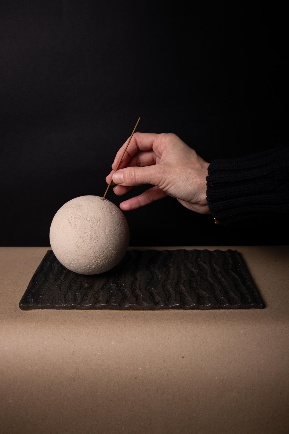 Hand placing an incense stick in a ceramic, textured sphere. Hand placing an incense stick in a design incense burner. Inspired by the full moon.
