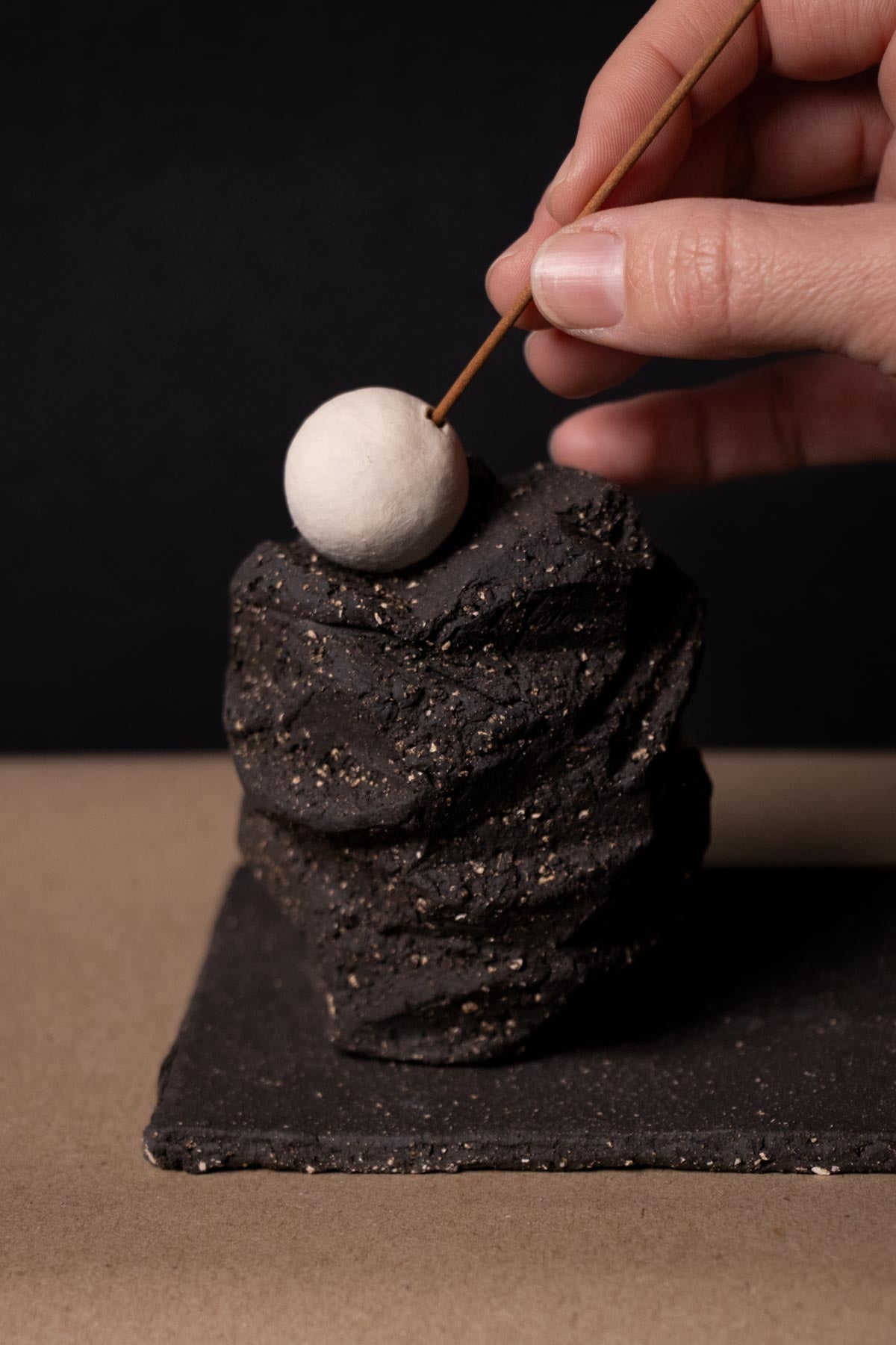 Hand placing an incense stick in a ceramic incense holder inspired by the moon. Kurinuki incense burner. Kurinuki ceramics.