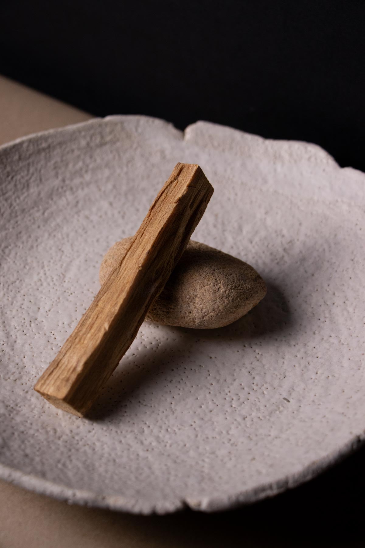 Palo santo stick lying on a pebble on a white textured ceramic plate. Decorative plate. Ritual dish.