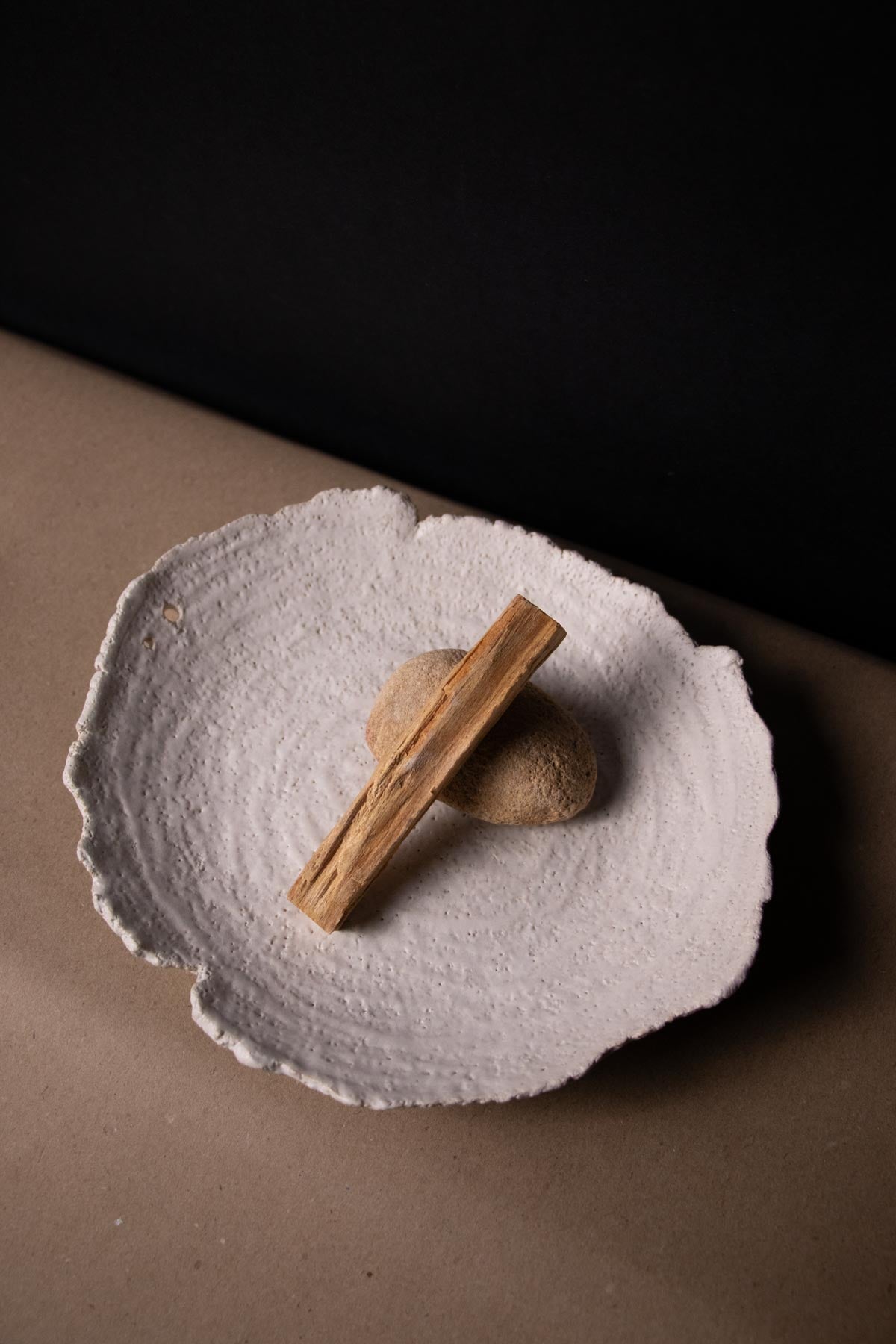 Palo santo stick lying on a pebble on a white textured ceramic plate. Ritual dish. Smudging ritual.
