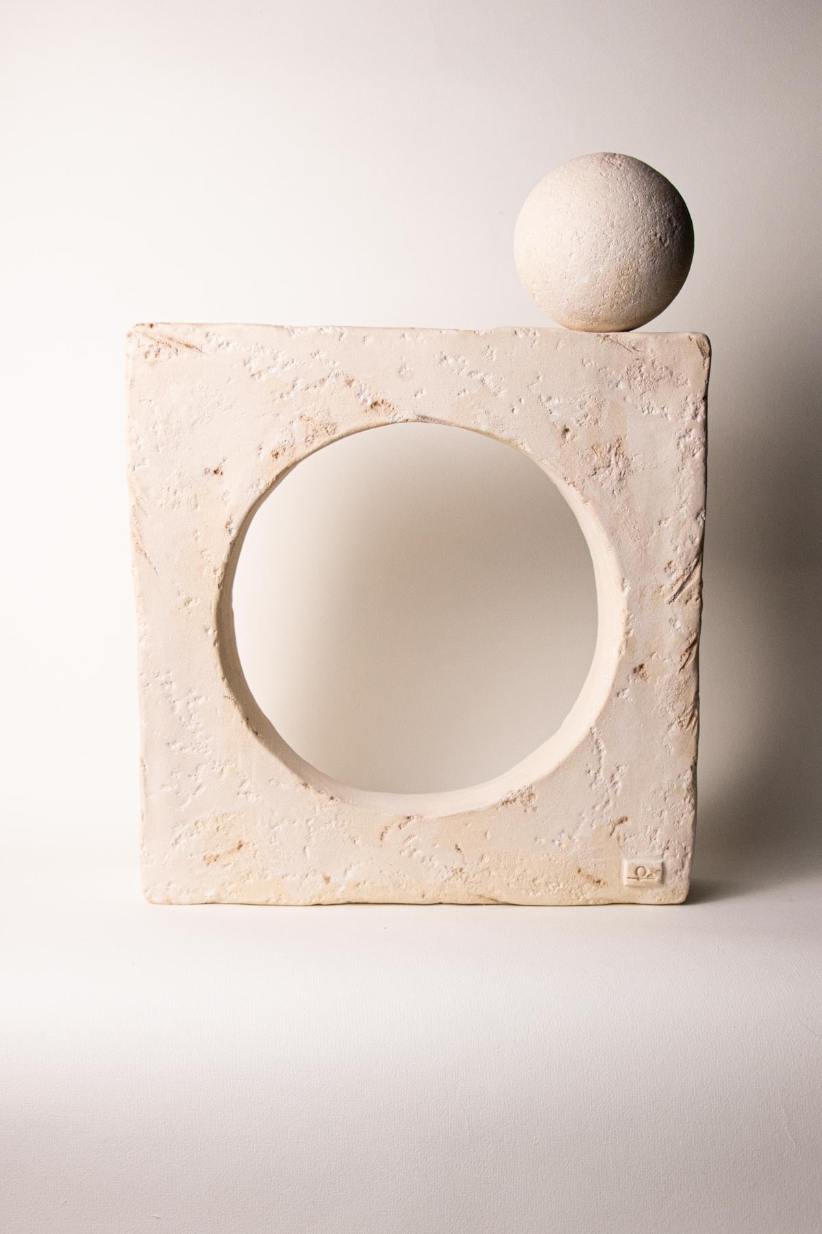 Ceramic square sculpture with a circular opening at the centre. on the top right corner there is a sphere that can be used as incense stick holder. Stoneware sculpture. Minimalist sculpture. Contemporary ceramics. Handmade ceramics. Organic texture. Cream and off-white colours. Neutral tones.