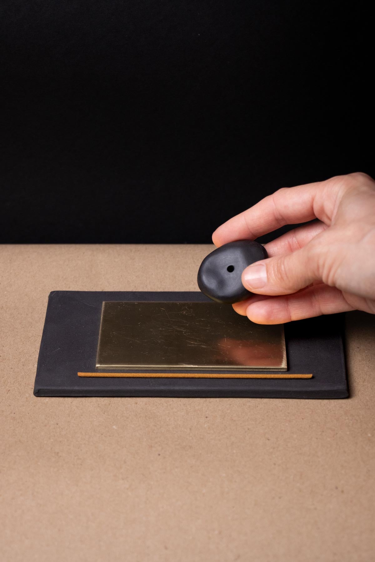 Hand holding a pebble like incense stick holder. Black porcelain. Contemporary ceramic incense holder. Brass incense burner. Minimalist design.