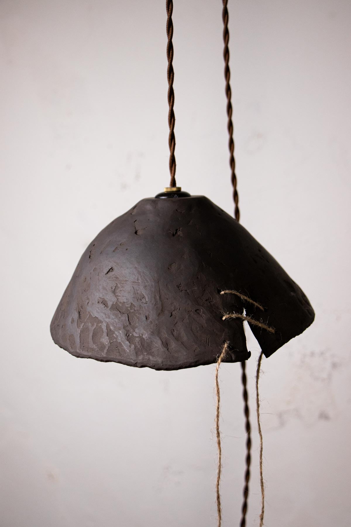 Dark brown, ceramic pendant lamp with exposed bulb against a light gray wall. Minimalist design. Handmade ceramic lamp. Handmade ceramics. Stoneware lamp.