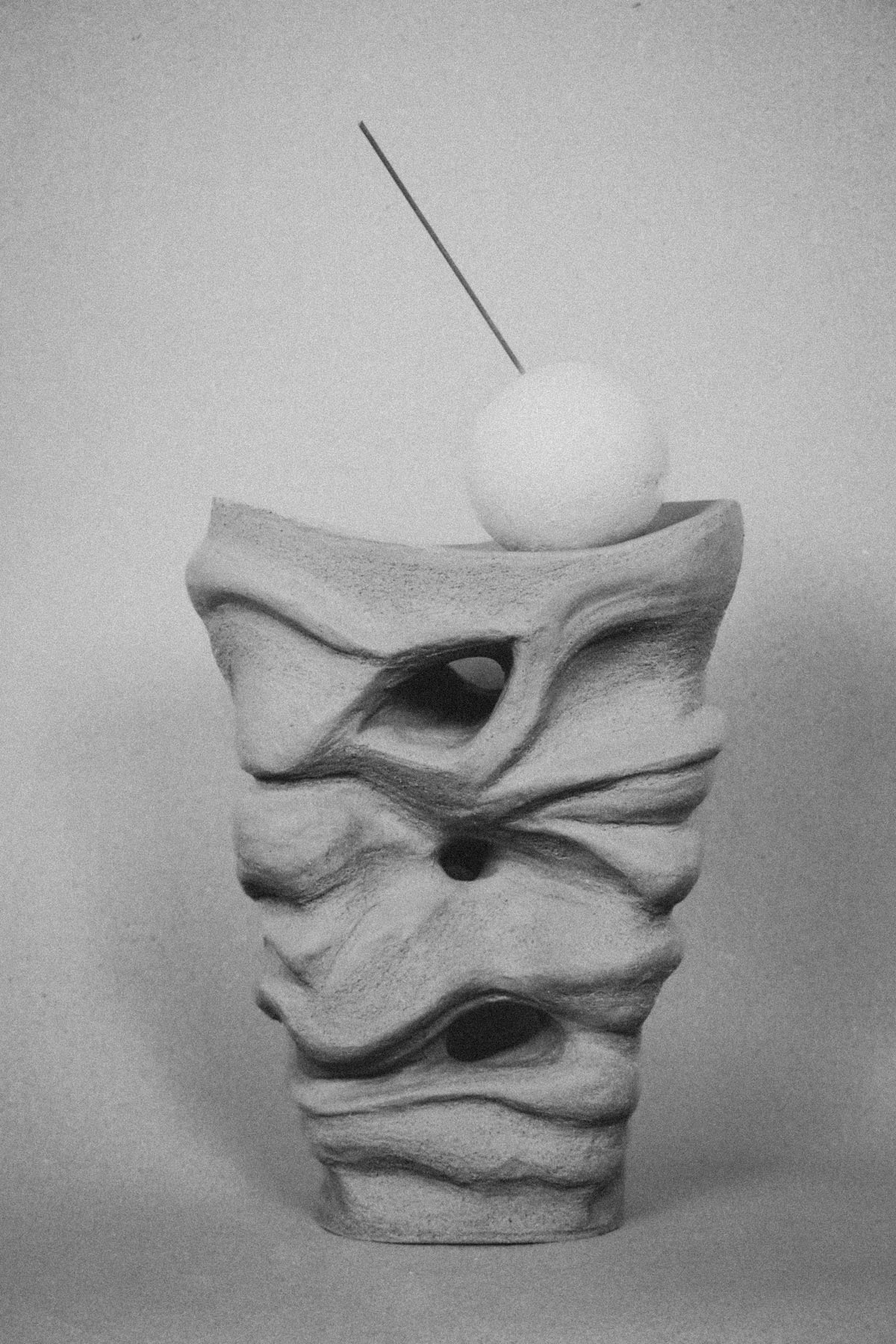 Abstract sculpture with wavy texture and spherical object on a gray background