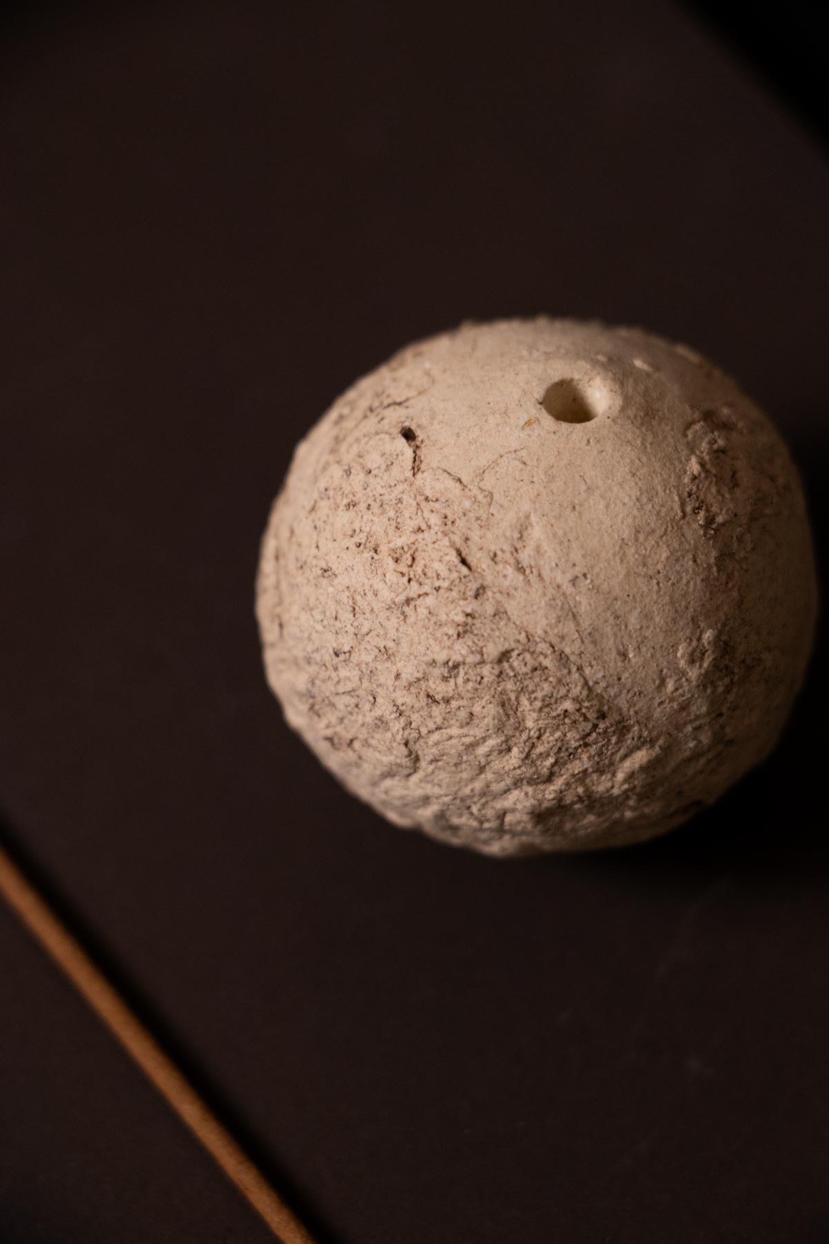 Textured cream ceramic sphere with a small hole on a dark background. Incense stick holder. Detail.