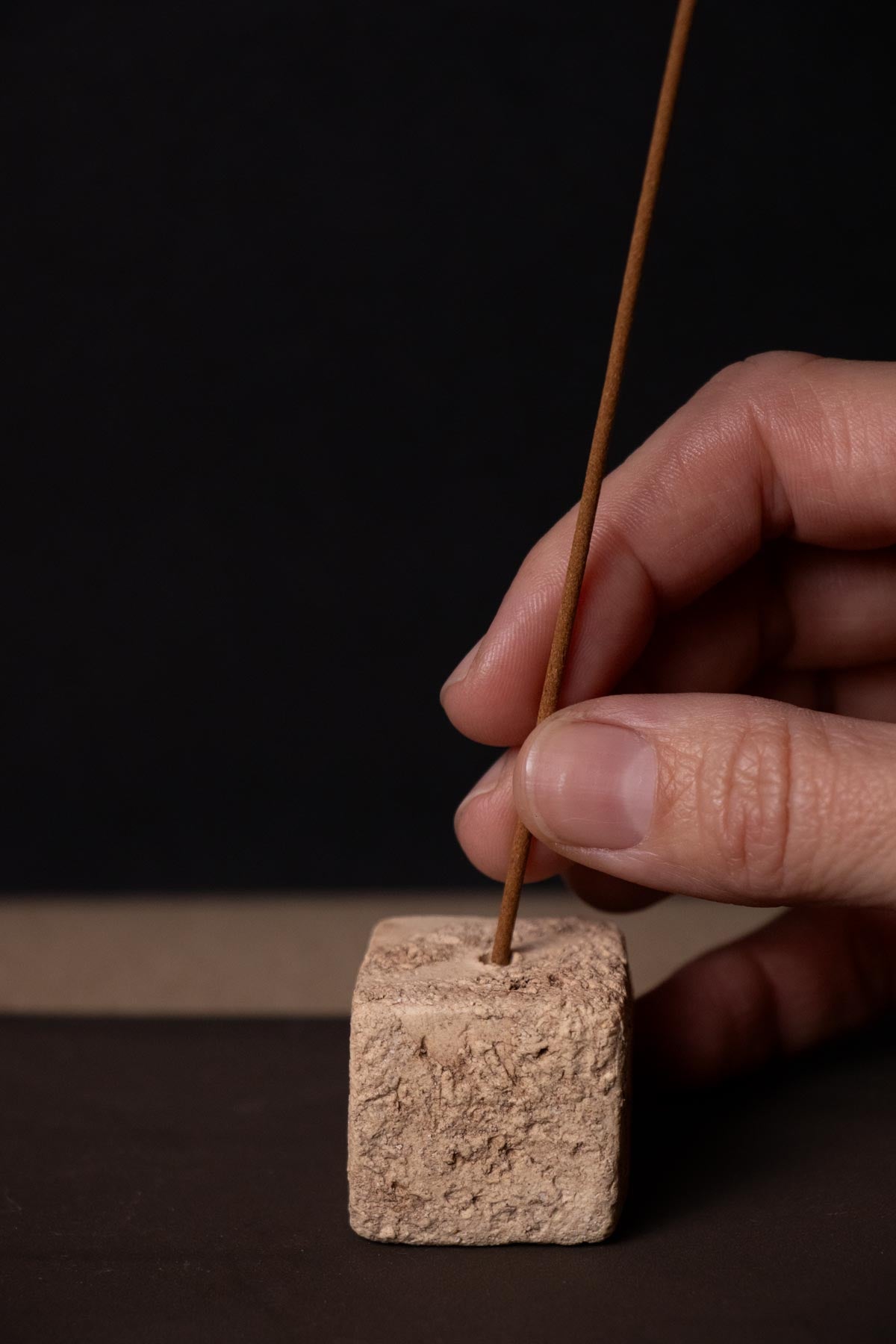 hand placing an incense stick in a textured ceramic cube. Cream and brown. Artistic incense burner. 