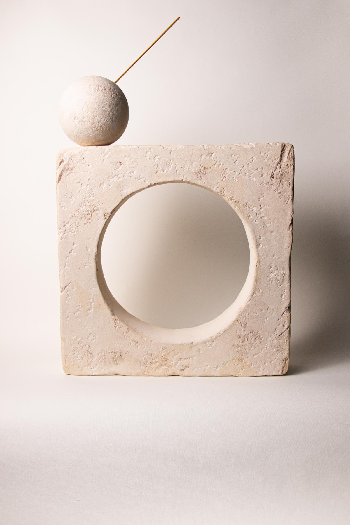 Ceramic square sculpture with a circular opening at the centre. on the top right corner there is a sphere that can be used as incense stick holder. Stoneware sculpture. Minimalist sculpture. Contemporary ceramics. Handmade ceramics. Organic texture. Cream and off-white colours. Neutral tones.
