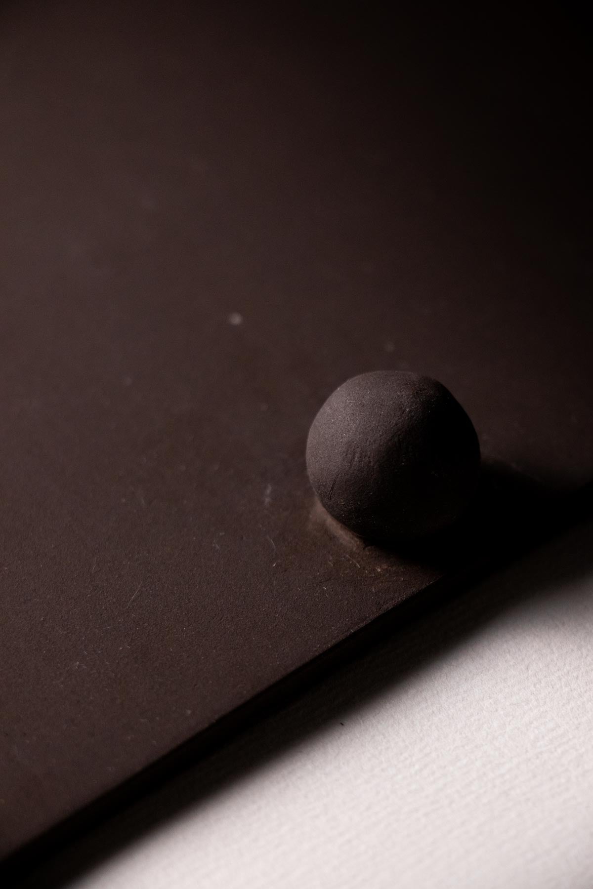 Dark brown sphere on a dark surface with a light source creating shadows