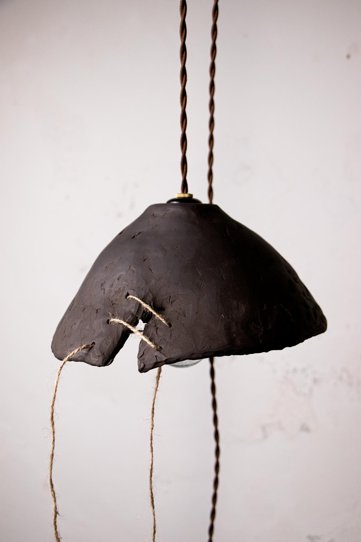 Dark brown, ceramic pendant lamp with exposed bulb against a light gray wall. Minimalist design. Handmade ceramic lamp. Handmade ceramics. Stoneware lamp. 