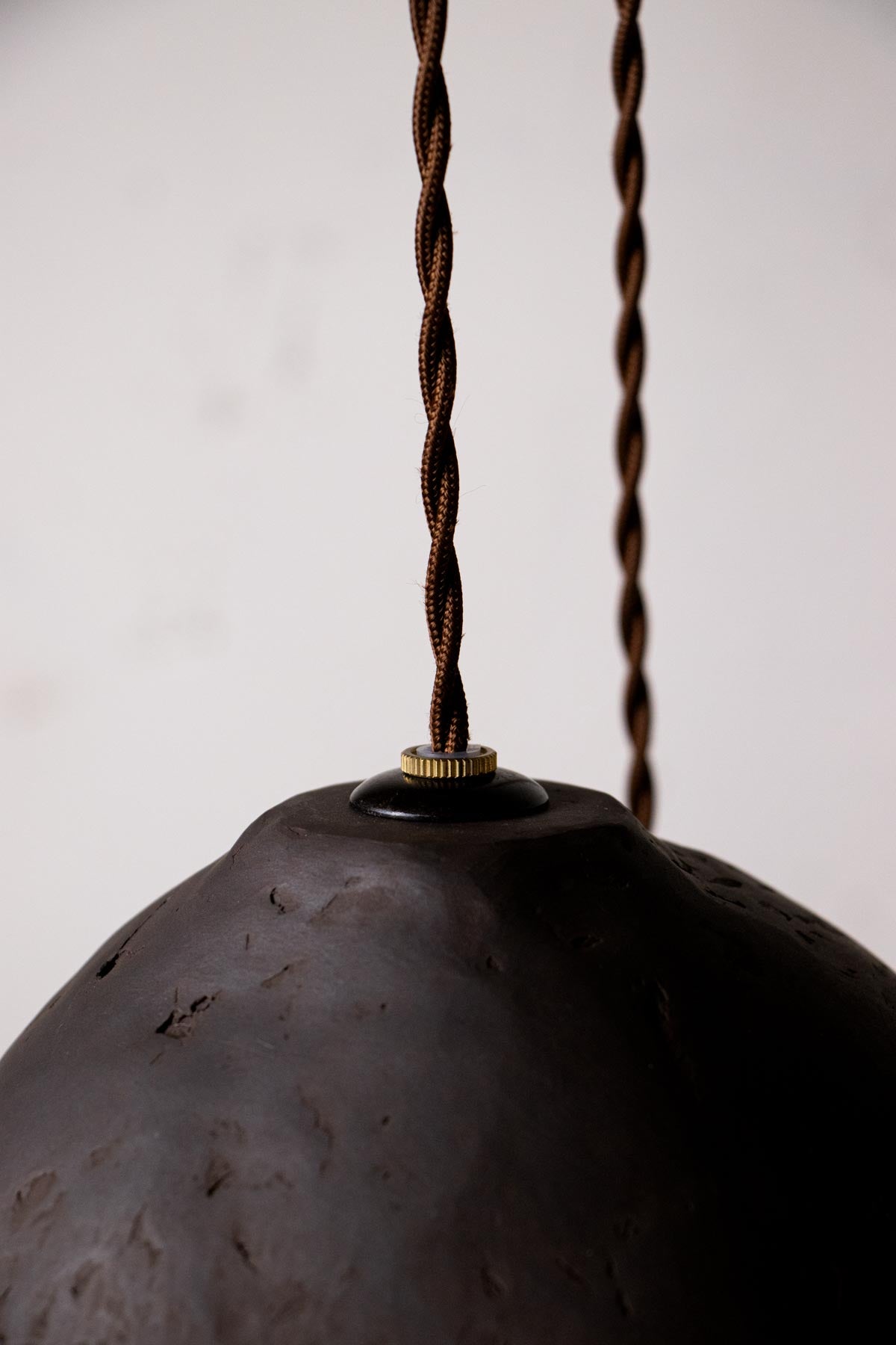 Close-up of a dark brown pendant light with twisted cord against a plain background