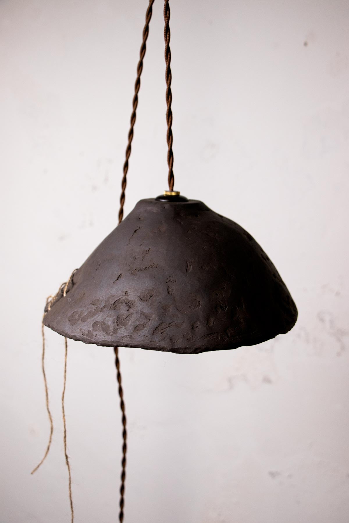 Dark brown, ceramic pendant lamp with exposed bulb against a light gray wall. Minimalist design. Handmade ceramic lamp. Handmade ceramics. Stoneware lamp. 