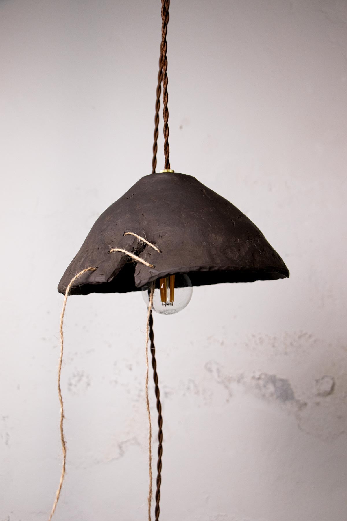 Dark brown, ceramic pendant lamp with exposed bulb against a light gray wall. Minimalist design. Handmade ceramic lamp. Handmade ceramics. Stoneware lamp. 