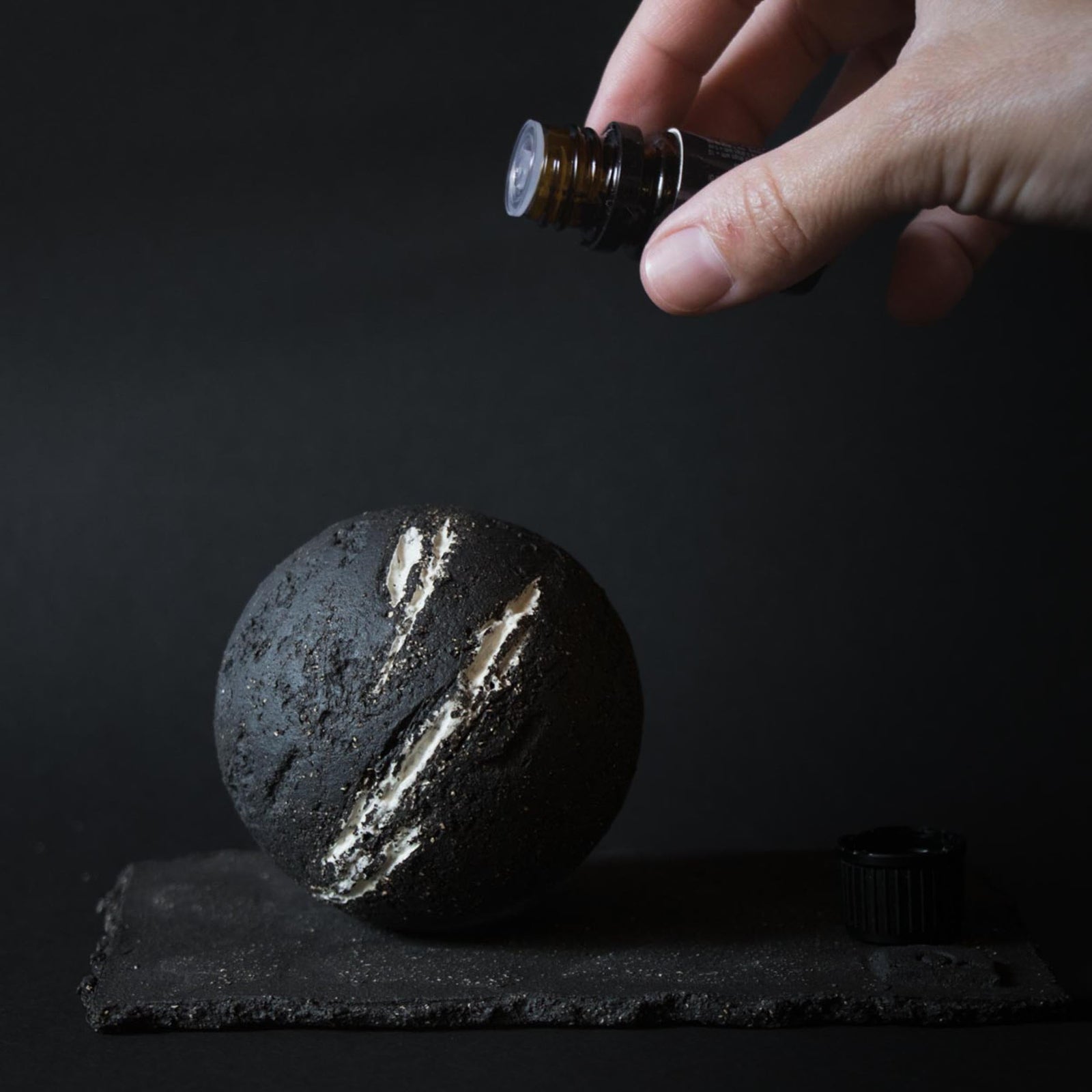 Hand dropping essential oil on a ceramic sphere diffuser on a dark background